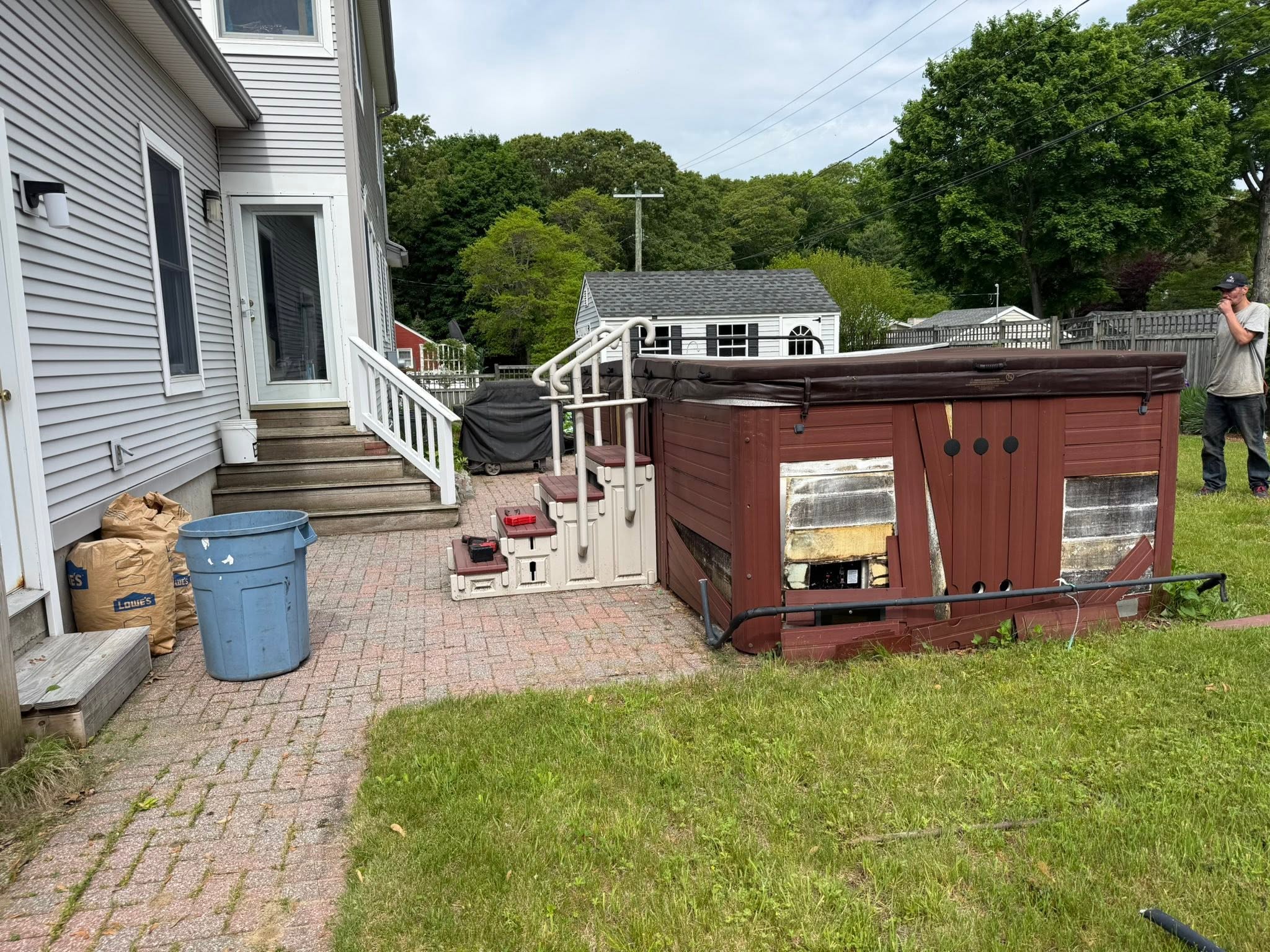 Backyard hot tub with damaged cabinet beside a patio before removal